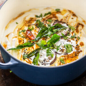 eggplant and yogurt dish garnished with curry leaves, cilantro and spices served in a round dutch oven