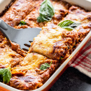 paneer lasagna in an orange color baking dish with a spatula scooping out a portion from the lasagna