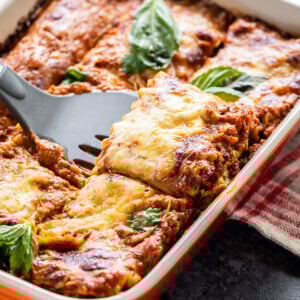 paneer lasagna in an orange color baking dish with a spatula scooping out a portion from the lasagna
