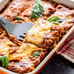 paneer lasagna in an orange color baking dish with a spatula scooping out a portion from the lasagna