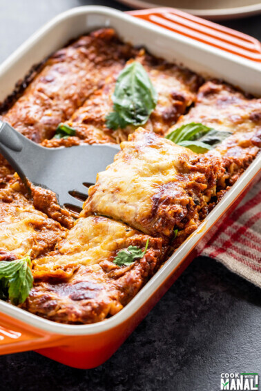 paneer lasagna in an orange color baking dish with a spatula scooping out a portion from the lasagna
