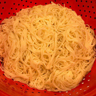 boiled noodles in a red color colander