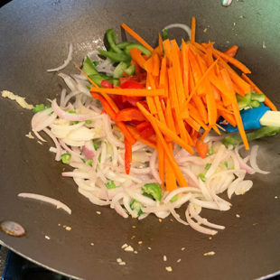 sliced carrots, peppers with sliced onion in a wok