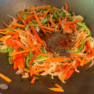 soy sauce, hot sauce being added to a wok with veggies