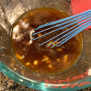 brown color sauce being whisked in a glass measuring jar