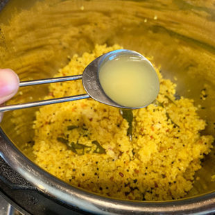 a tablespoon of lemon juice being added to a pot pf quinoa