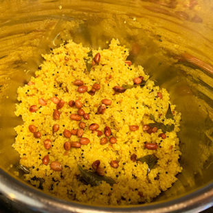 yellow color quinoa in a steel pot topped with roasted peanuts