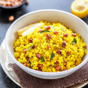 white bowl with yellow color quinoa topped with peanuts, with a wedge of lemon in the background along with a bowl of peanuts