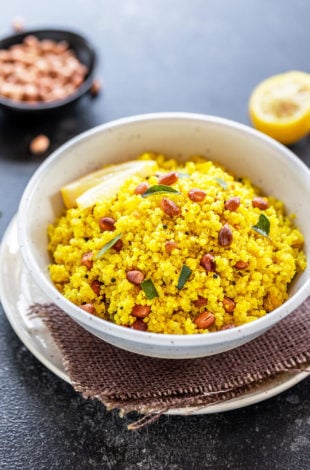 white bowl with yellow color quinoa topped with peanuts, with a wedge of lemon in the background along with a bowl of peanuts