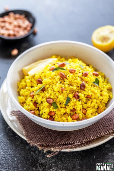 white bowl with yellow color quinoa topped with peanuts, with a wedge of lemon in the background along with a bowl of peanuts