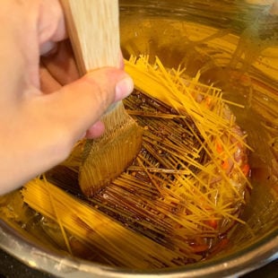 a wooden spatula pressing spaghetti noodles arranged in a criss-cross manner in an instant pot