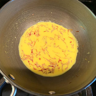 a small pan with milk and saffron strands making the milk yellow in color