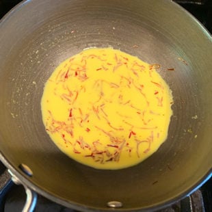 a small pan with milk and saffron strands making the milk yellow in color