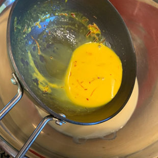 a small pan with yellow color saffron milk being added to a bowl