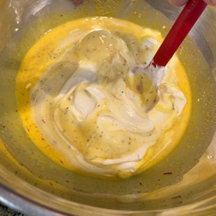 whipped cream being folded in a condensed milk mixture using a red spatula