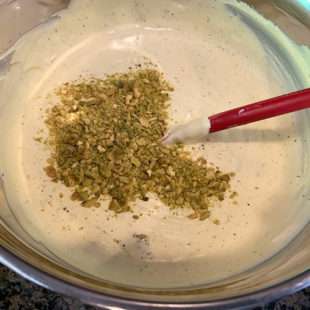 crushed pistachios being added to an ice cream mixture in a large bowl