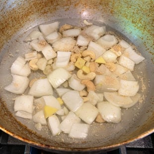 a kadai/wok filled with onion, cashews, ginger, garlic in water