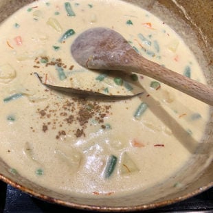 wok with veggies in a white color sauce and ground spice sprinkled on top