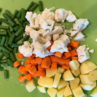 a green mat with chopped potato, cauliflower, beans, carrot placed on it