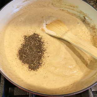 ground black pepper being added to a white color sauce in a pan