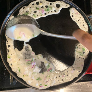 a white color thin batter being poured on an iron skillet