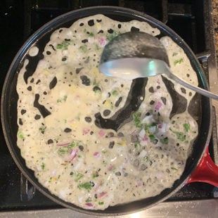 a white color thin batter being poured on an iron skillet
