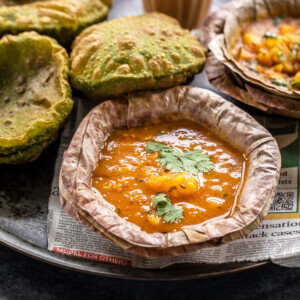 potato curry served in a traditional Indian leaf bowl and puris and chai placed in background
