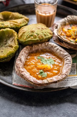 potato curry served in a traditional Indian leaf bowl and puris and chai placed in background