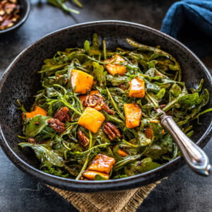 bowl of mango arugula salad with a fork placed in the bowl and another plate of salad in the background