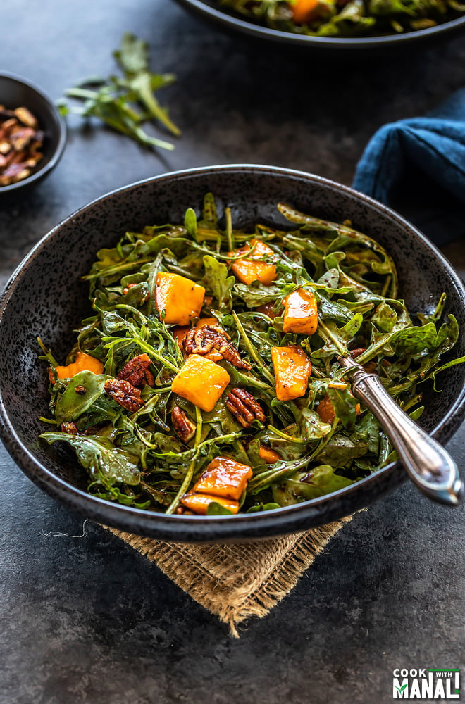 bowl of mango arugula salad with a fork placed in the bowl and another plate of salad in the background