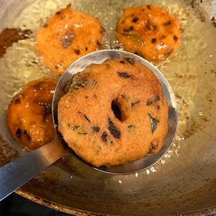 golden brown fried vada being removed from hot oil with a spatula