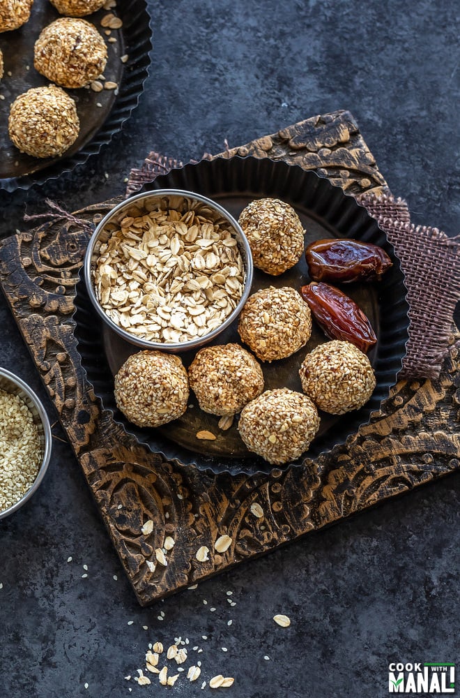 sesame oats balls placed in a plate with 2 medjool dates placed on one side and bowl of oats on the other side