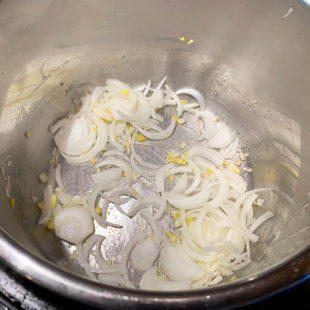 sliced onion, chopped garlic and ginger being sauteed in a pot