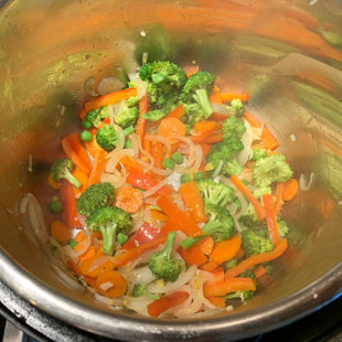 broccoli florets, sliced red pepper, carrots and green peas in a pot