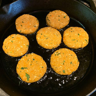 sweet potato tikkis being fried in oil in a cast iron skillet