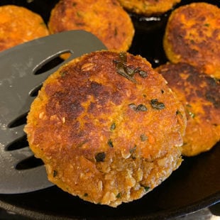 golden brown sweet potato tikki being taken out of a skillet using a spatula