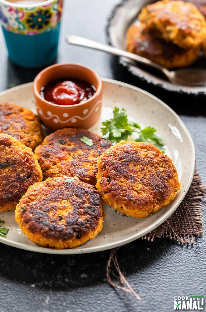 sweet potato tikki served in a while plate with a twig of cilantro and a bowl of ketchup on the side