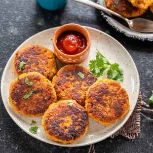 sweet pottao tikki arranged in a white plate with a small bowl of ketchup on the side a glass of chai placed in the background