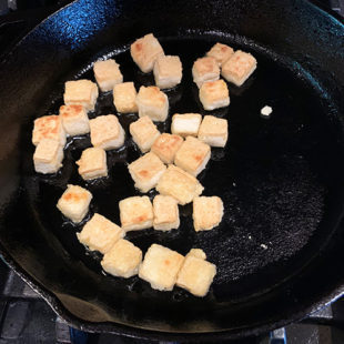 tofu being cooked on a cast iron skillet