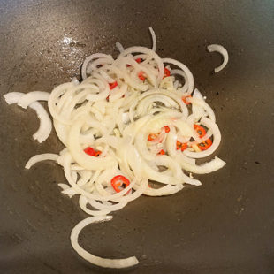 sliced onion, garlic and red thai pepper in a wok