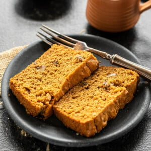 two slices of whole wheat jaggery cake in a plate with a cup of chai in the background