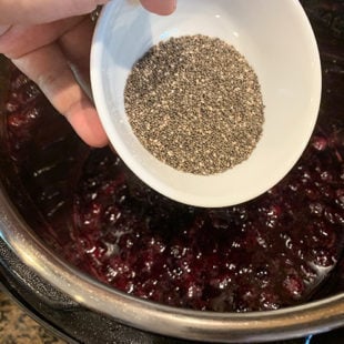 chia seeds being added to a pot of blueberries