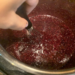 a wire whisk whisking blueberry jam in the instant pot