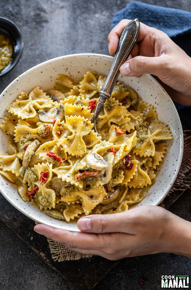 pair of hands holding a bowl of bow tie pasta with mushrooms and sun-dried tomatoes