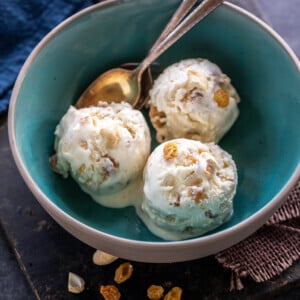 3 scoops of white color ice cream topped with cashews and raisins and served in a blue color bowl