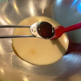 vanilla extract being added to a bowl of condensed milk