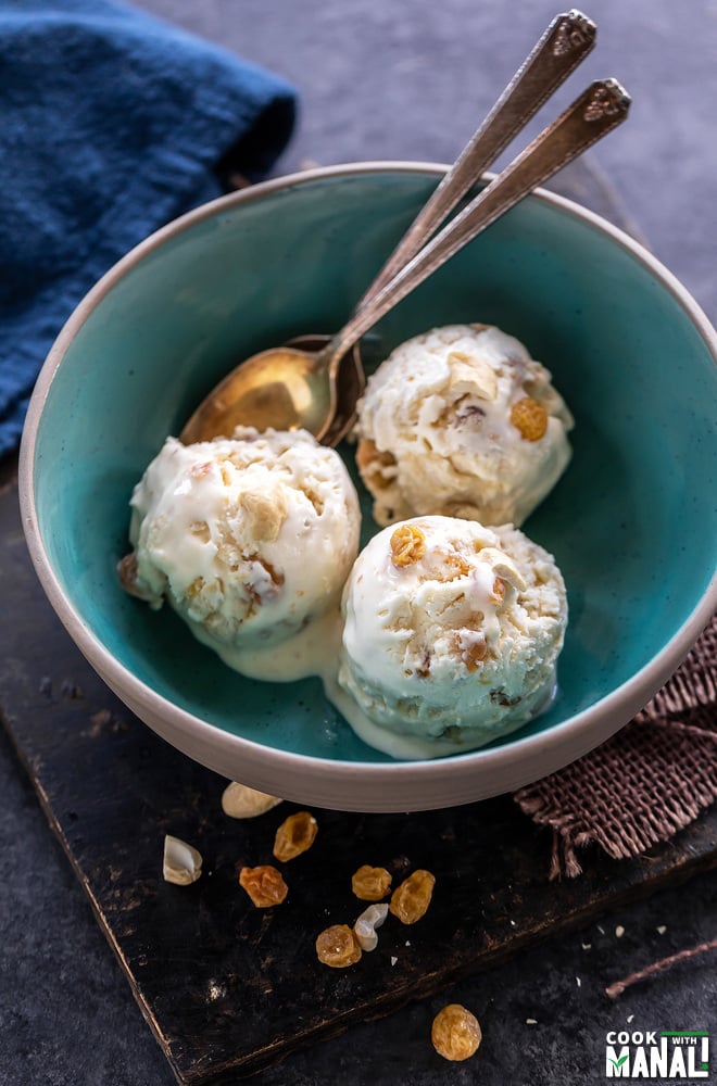 3 scoops of white color ice cream topped with cashews and raisins and served in a blue color bowl