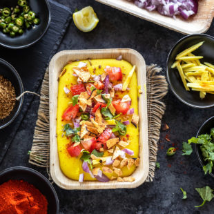 moong dal chaat served in a rectangular serving bowl topped with tomatoes, onion and bowls of cilantro, chili powder, onion, tomatoes placed in the background and on the sides