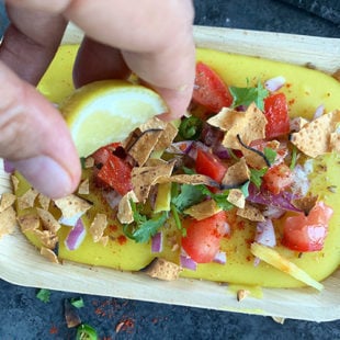 hand squeezing lemon juice onto a plate of moong dal topped with onion, tomatoes, cilantro