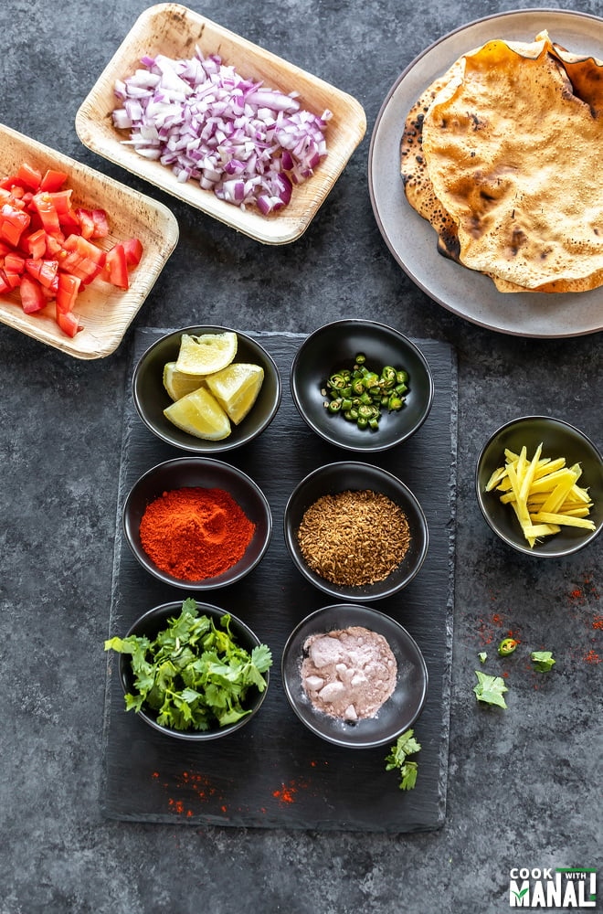 6 bowls arranged on a black cheese board containing cilantro, ginger julienne, cumin powder, rock salt, green chilies and lemon wedges